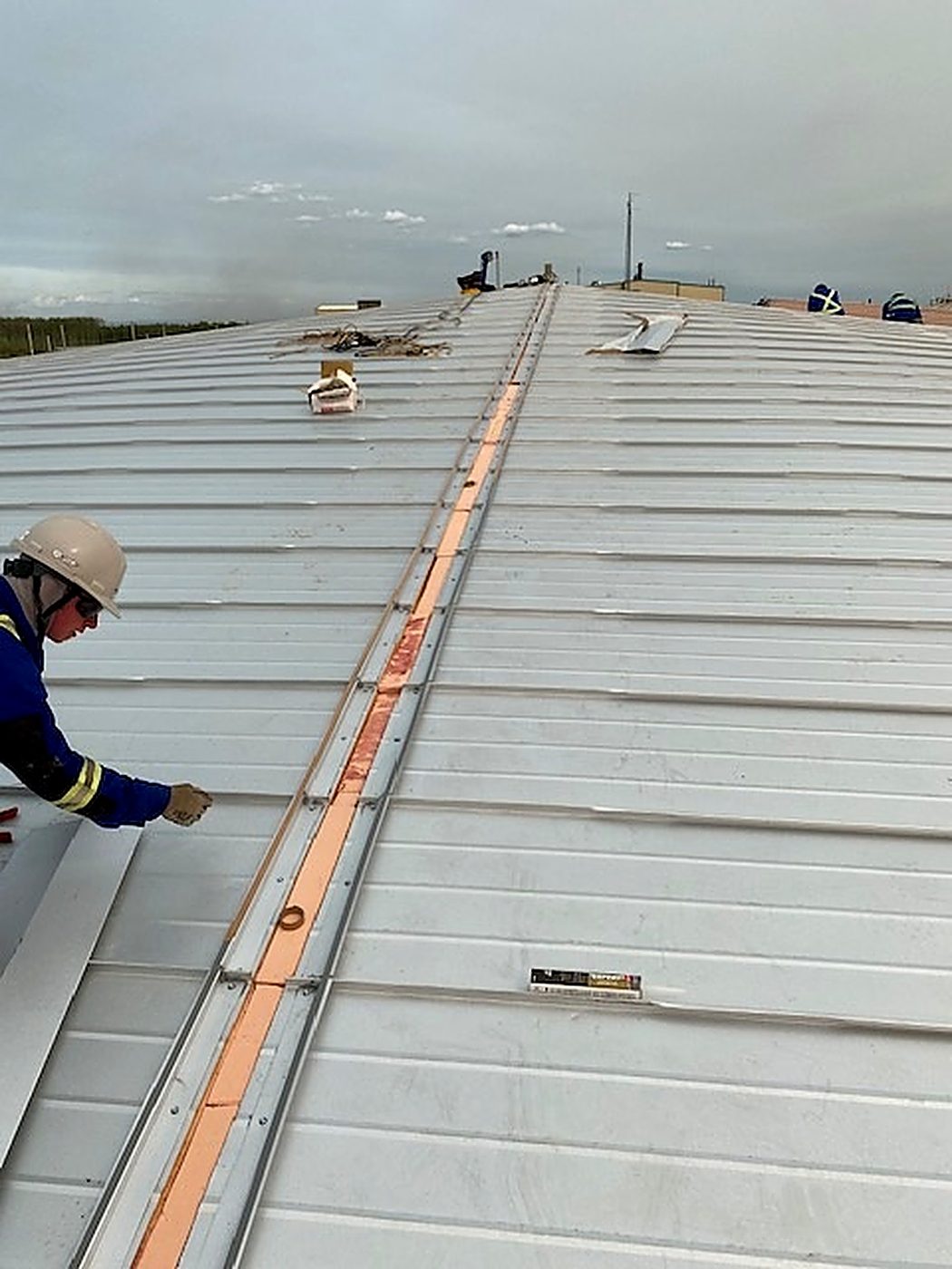 Standing-seam panel runs meeting at the roof centre with the polyiso core visible in the open joint