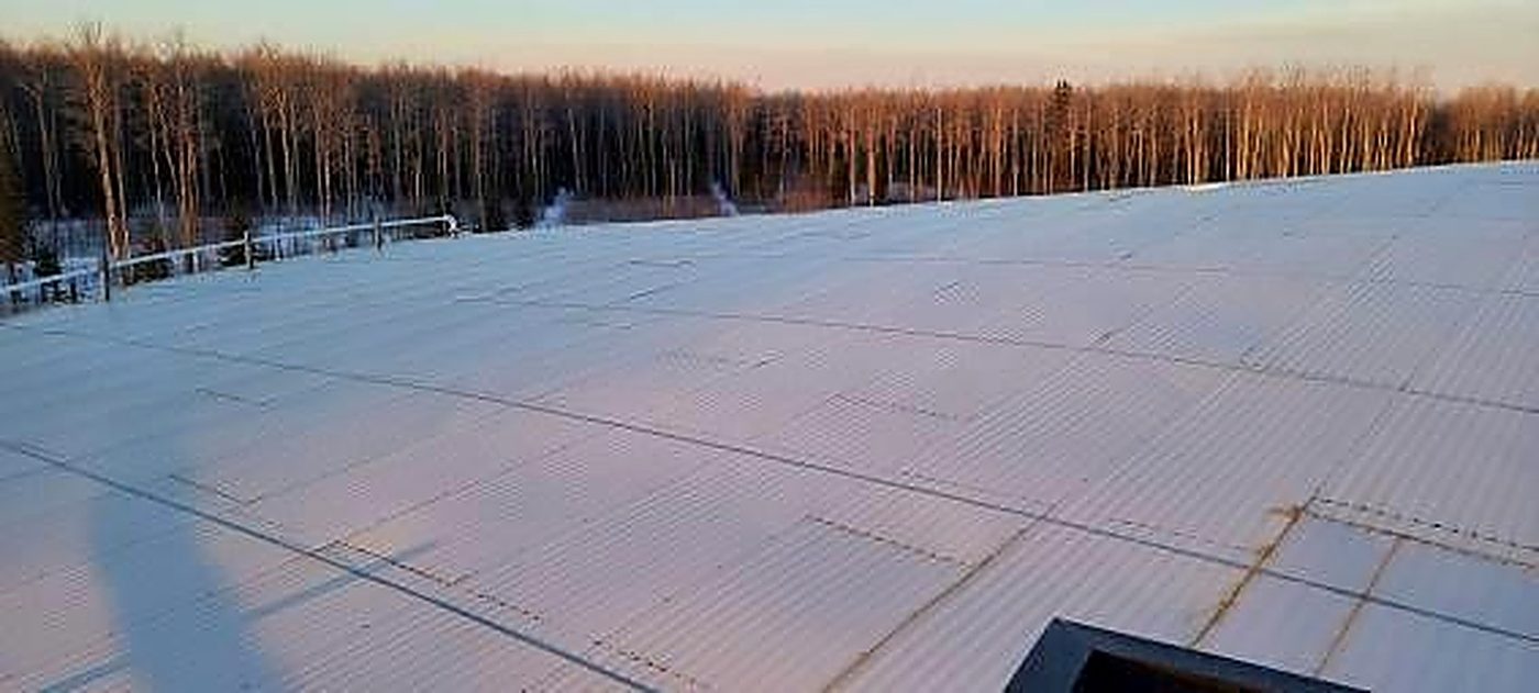 Existing corrugated lap-and-fastener roof jacketing on a storage tank, overlap lines and patch repairs across the full field