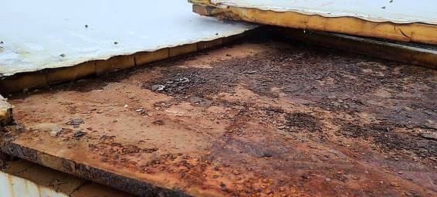 Lifted lap edge on the old roof exposing wet, degraded insulation and corrosion staining